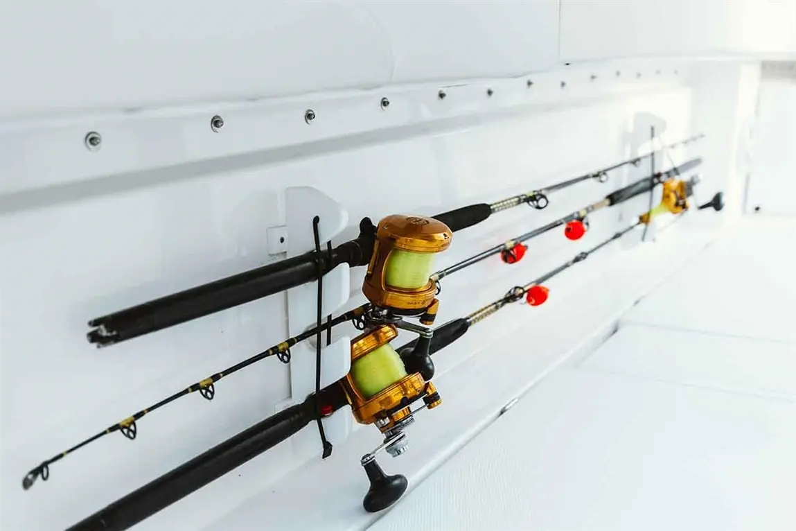 Two fishing rods with gold reels mounted on a white wall, showcasing vibrant red bobbers and a sleek boat interior.